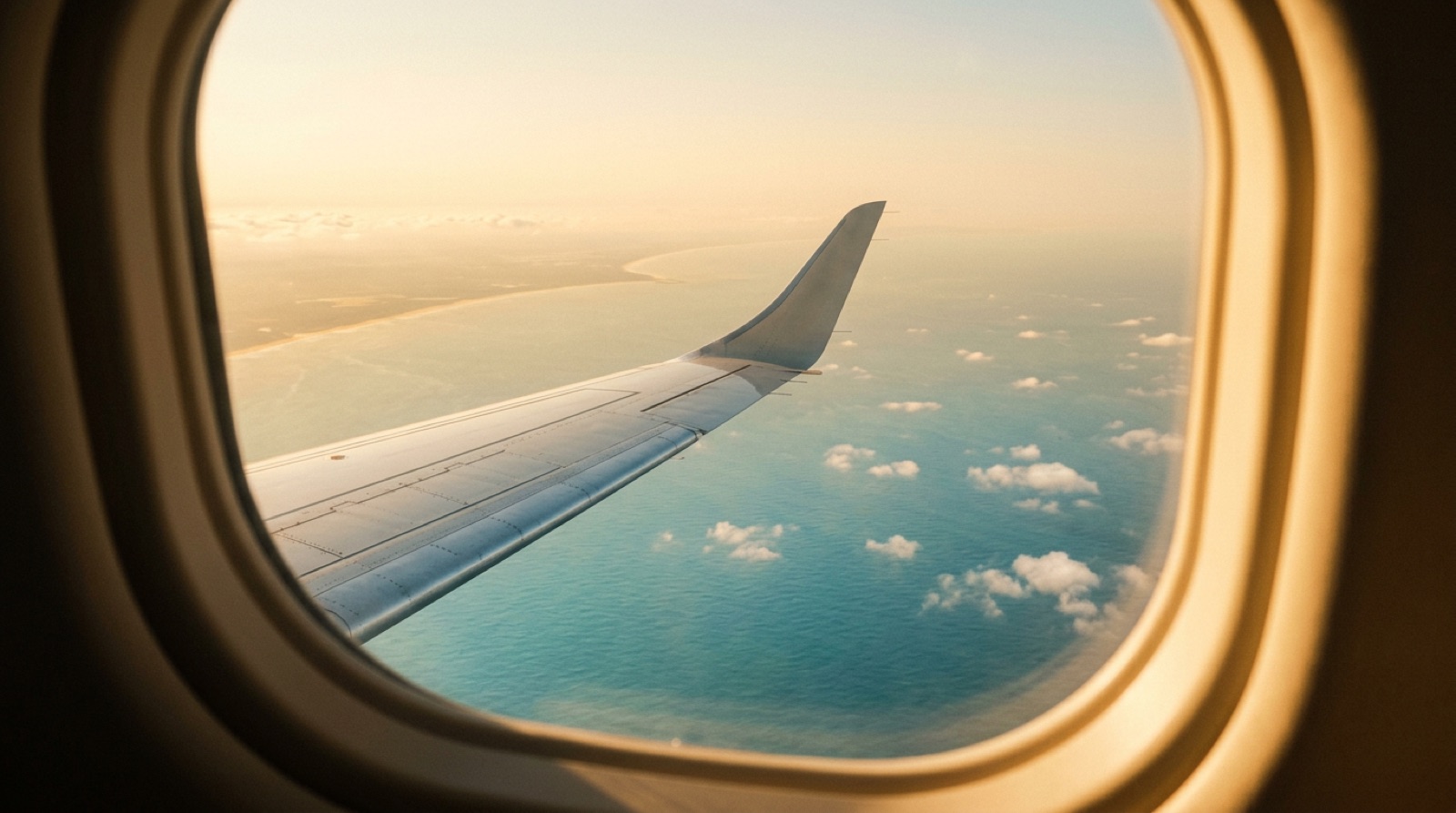 Private jet wing over a sunlit sea and distant coastline at golden hour